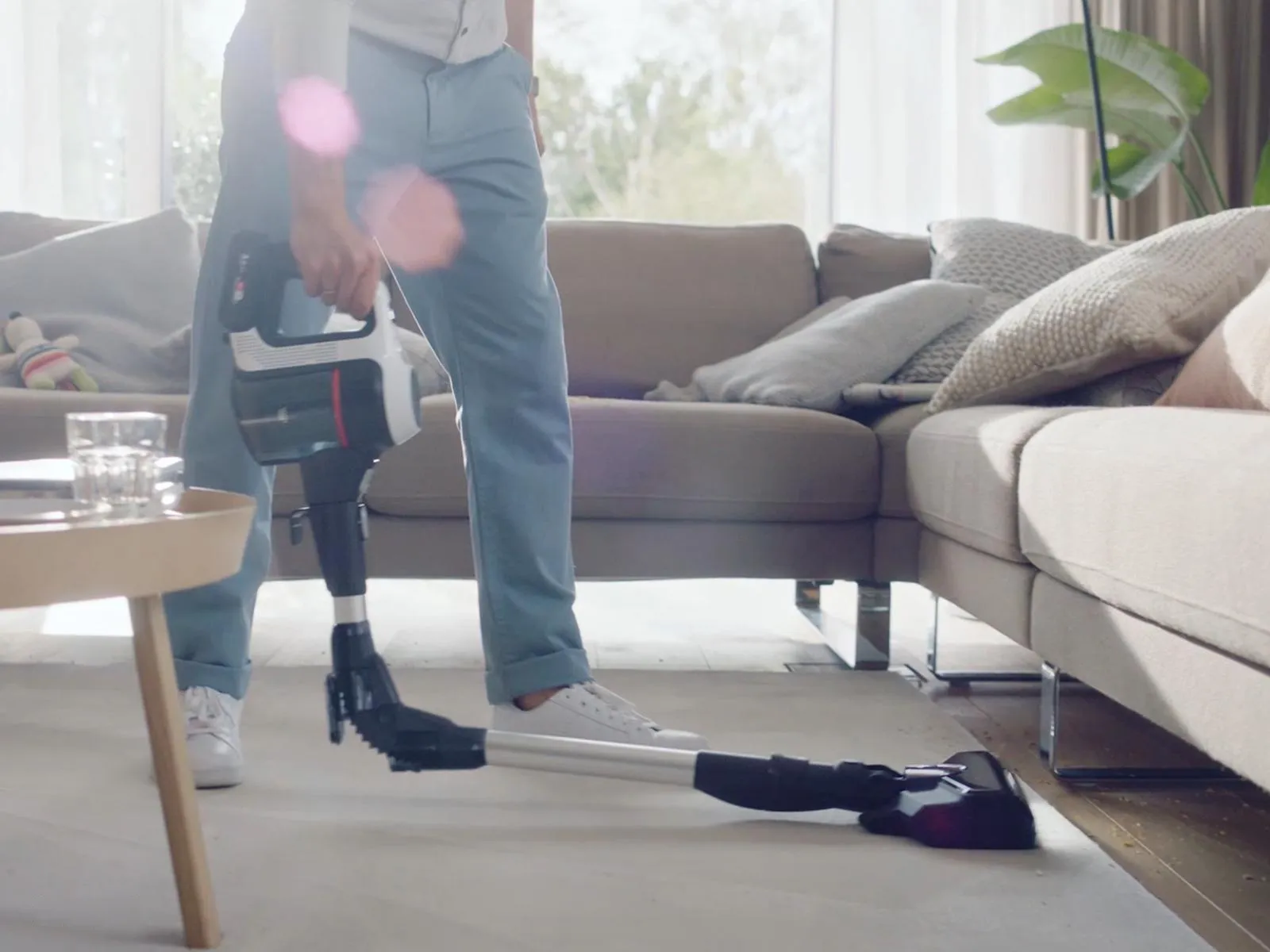 Person with a prosthetic leg vacuuming the floor in a bright living room with modern furniture and plants.