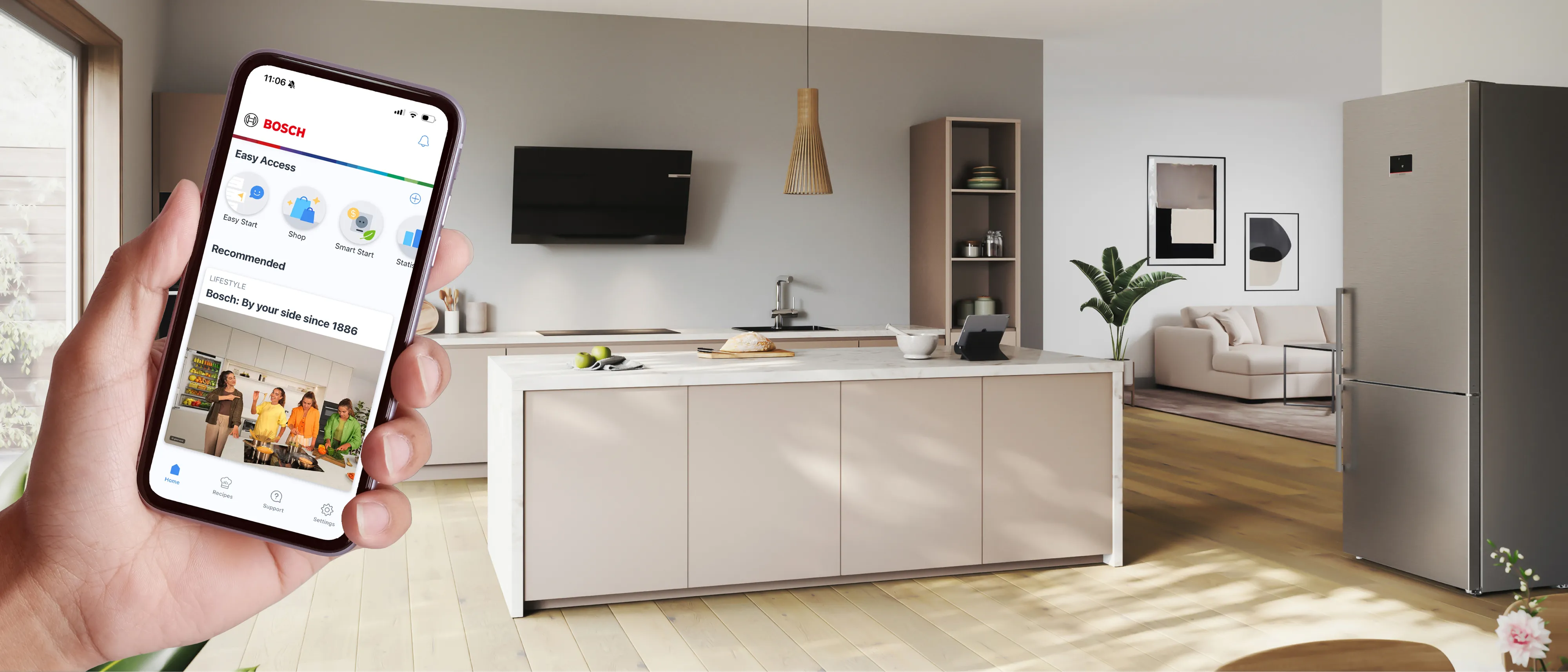 A hand holding a smartphone in the foreground, with a cozy kitchen scene in the background.
