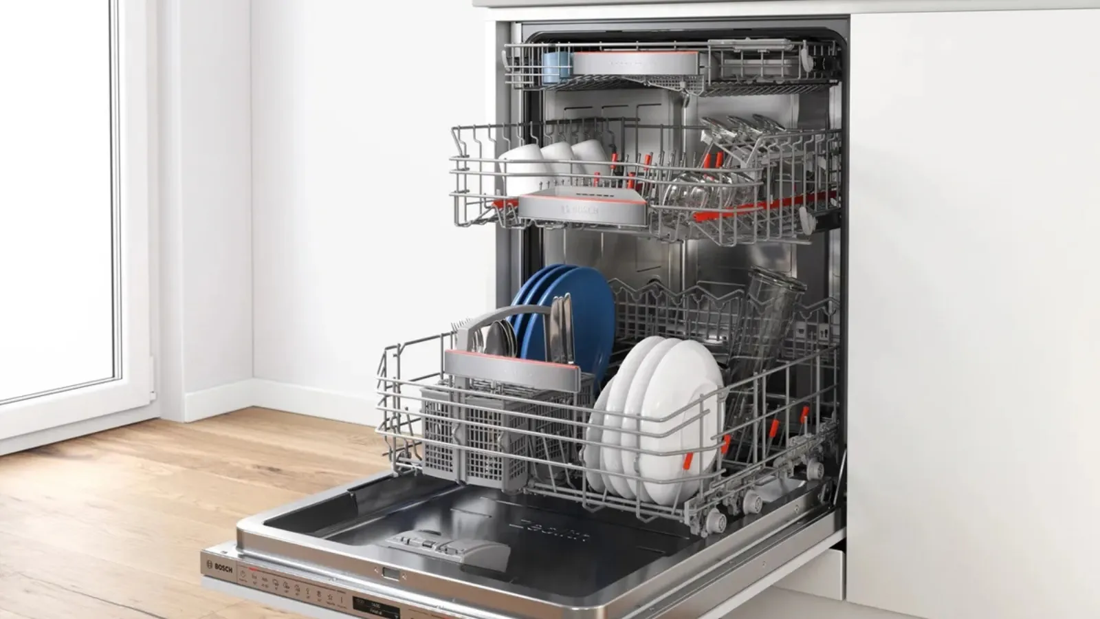 Lavavajillas abierto y cargado con platos, tazas, vasos y cubiertos en una cocina blanca moderna.