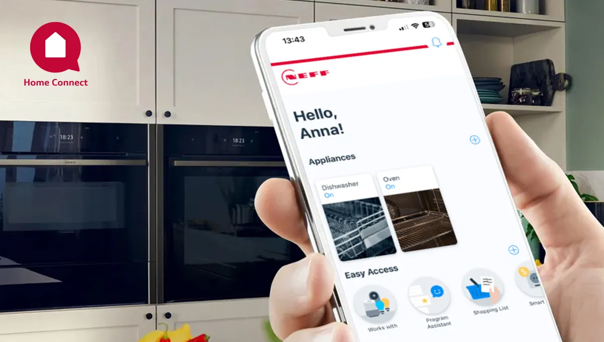 Ένα χέρι κρατάει ένα smartphone που δείχνει την εφαρμογή Home Connect μπροστά από ένα σύνολο εντοιχιζόμενων φούρνων.