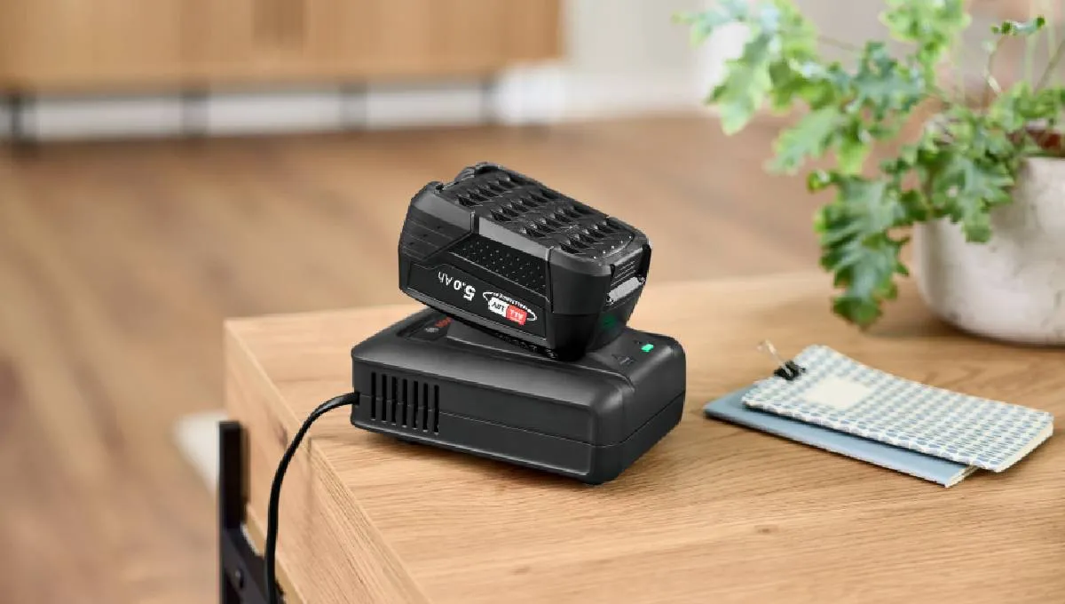 Black 5.0 Ah Bosch vacuum battery on its charging dock on a wooden table.