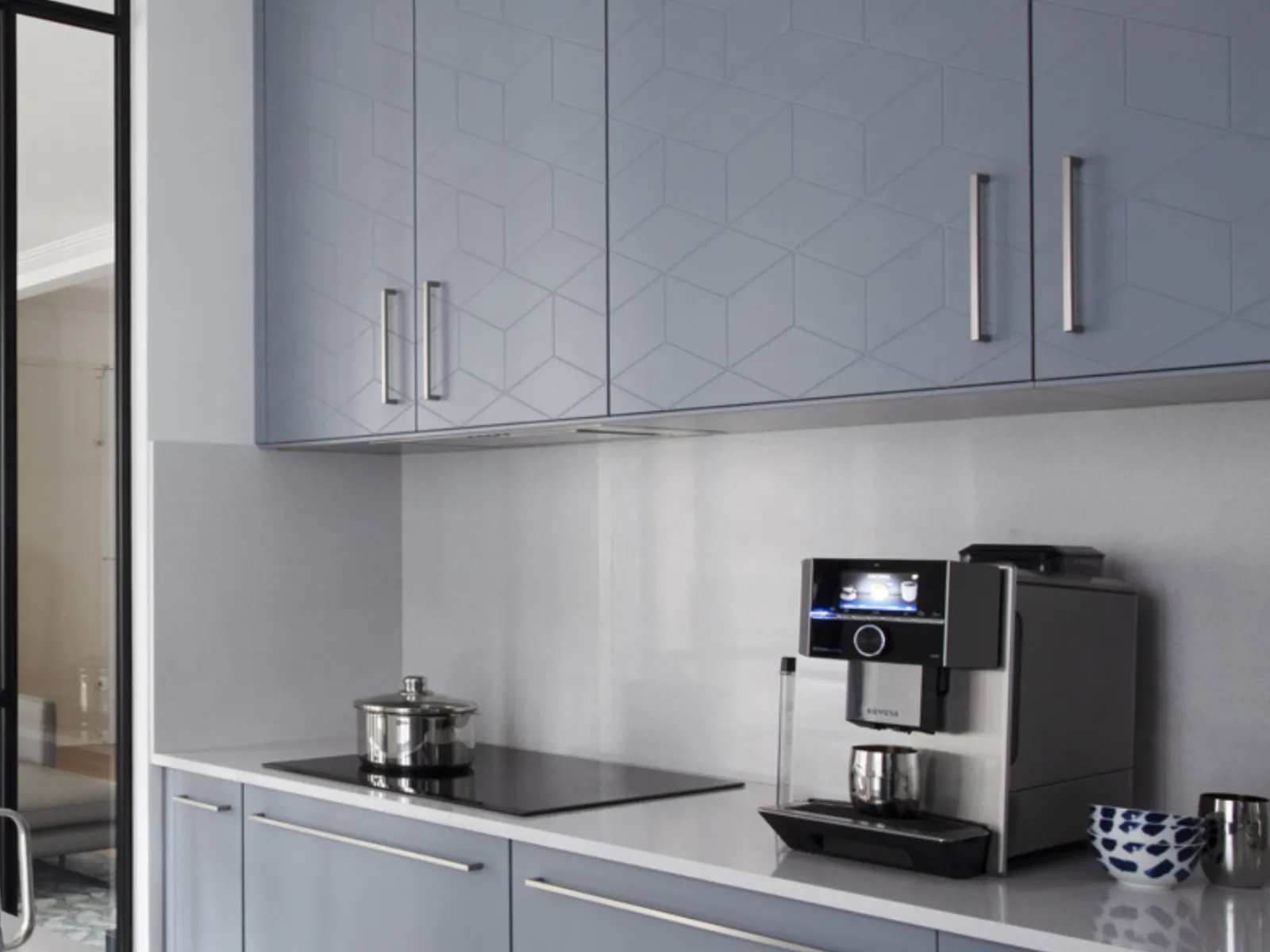 Cucina moderna con armadi grigi, elettrodomestici in acciaio inossidabile e parete divisoria in vetro.