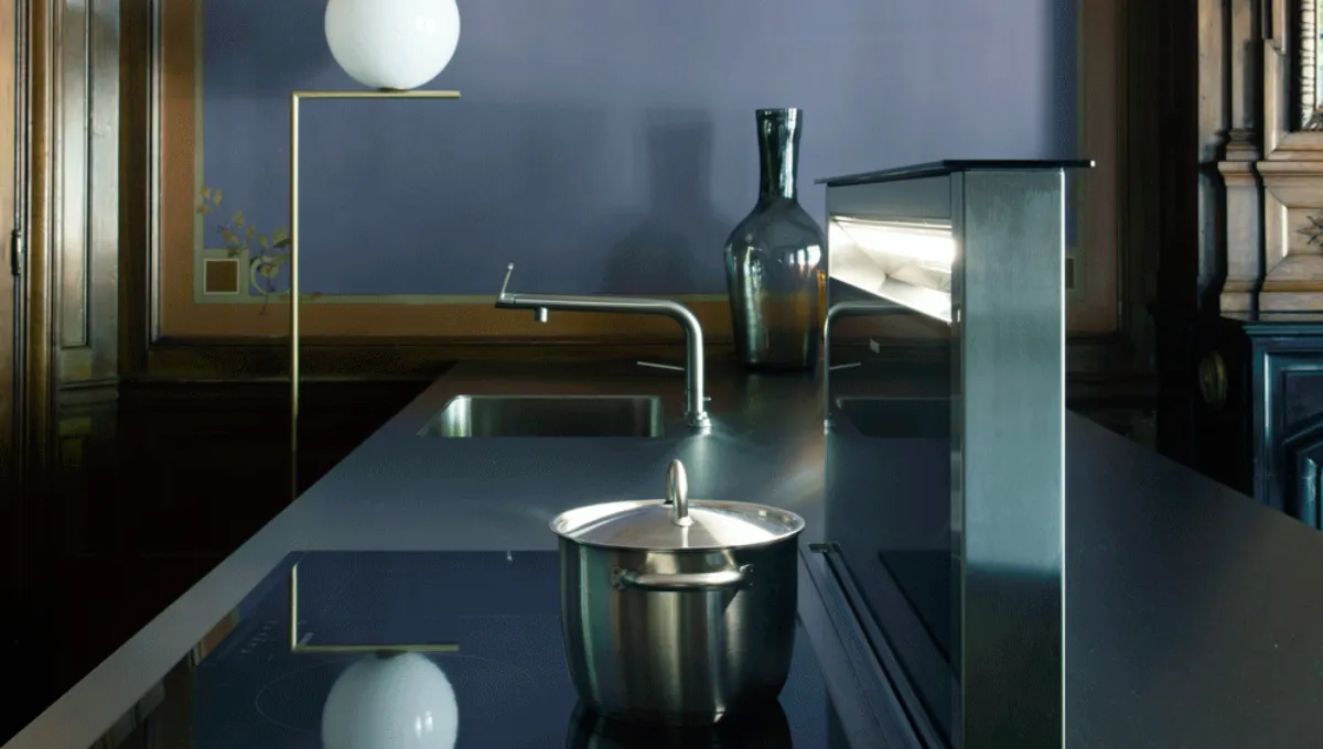 Moderna isola da cucina scura con lavello, rubinetto curvo, contenitore in acciaio inox, bottiglia di vetro e vetrina illuminata.