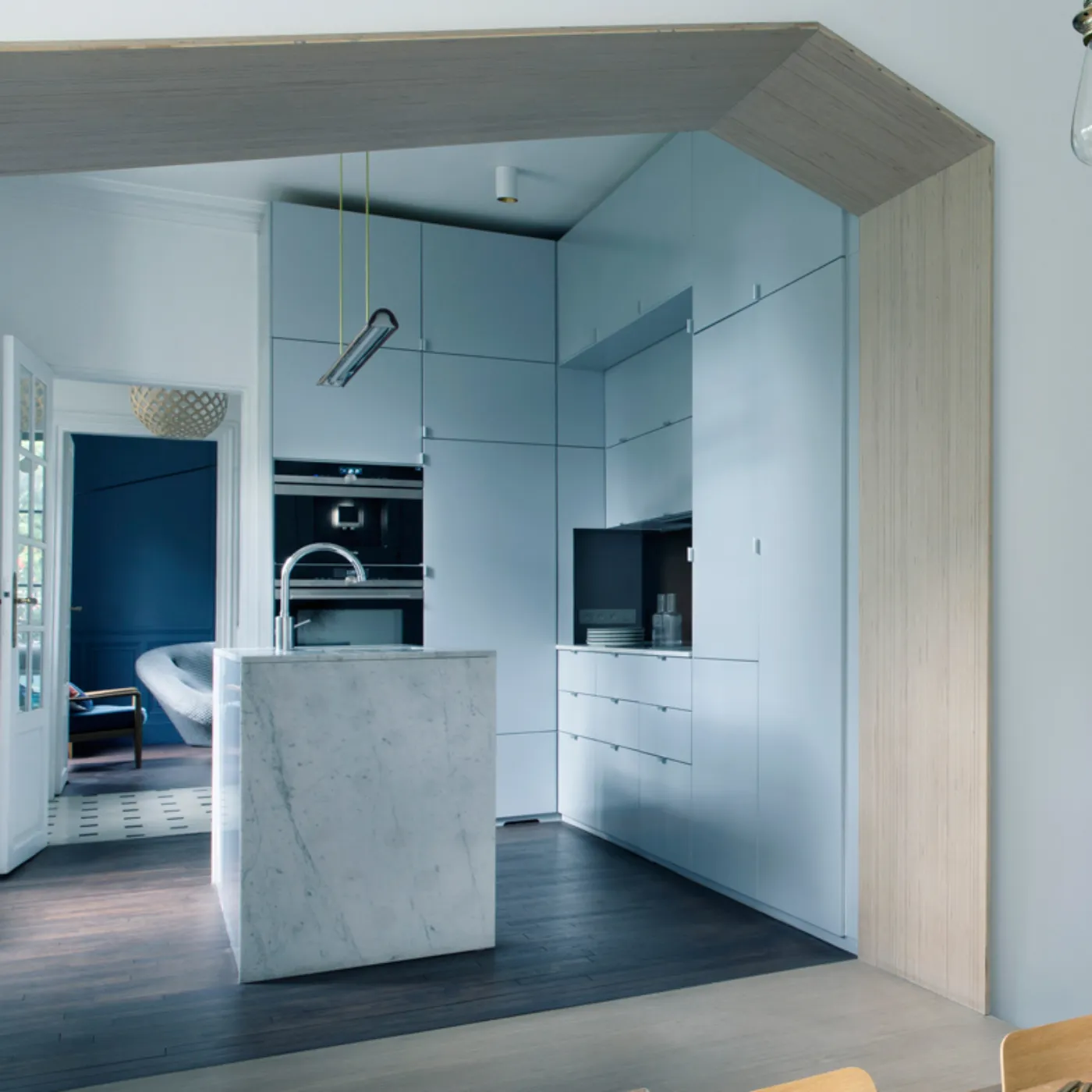 Cucina moderna con piano in marmo, luci a sospensione e tavolo da pranzo in legno con piatti colorati.