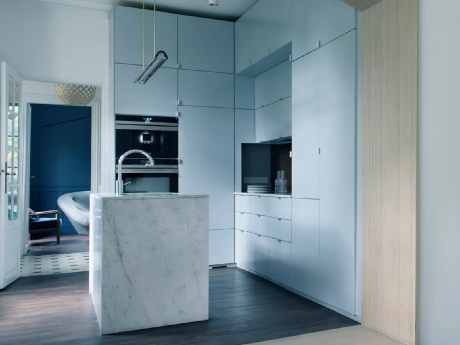 Cucina moderna con piano in marmo, luci a sospensione e tavolo da pranzo in legno con piatti colorati.