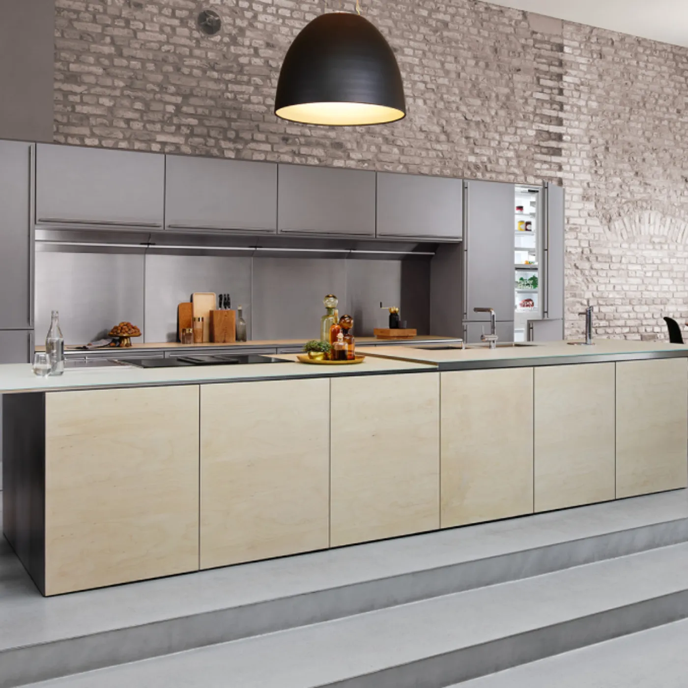 Cucina moderna con mobili grigi, elettrodomestici in acciaio inossidabile e pareti in mattoni a vista.