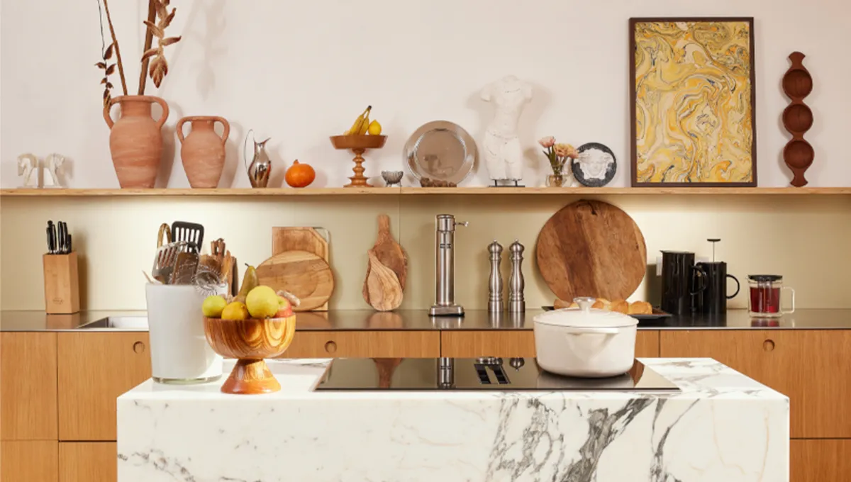 A front-on view of a designer kitchen, featuring a striking white marble island with a NEFF induction hob, wooden cabinetry, and an open shelf above displaying an eclectic mix of art, terracotta vases, and sculptures.