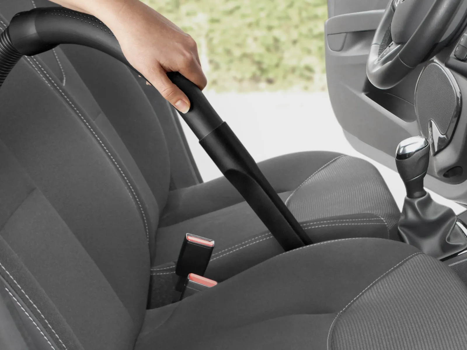 Primo piano di una persona che pulisce il sedile di un'auto con la bocchetta a lancia lunga di un aspirapolvere Bosch.