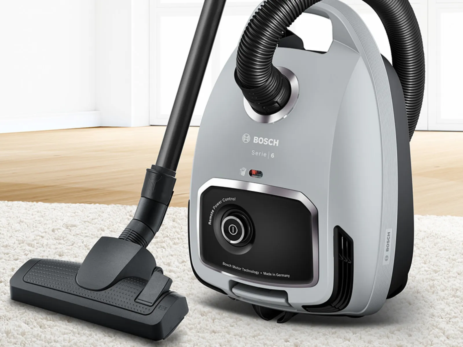 Primo piano dell'aspirapolvere a traino con sacco Bosch Serie 6 grigio, su un tappeto bianco.