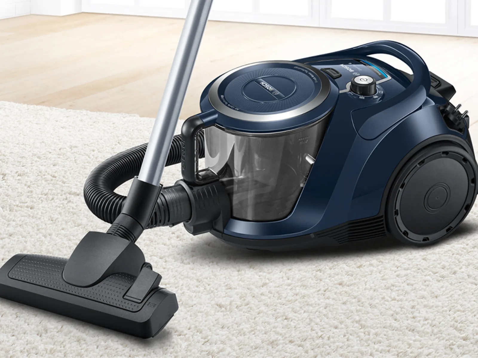 Primo piano dell'aspirapolvere a traino senza sacco Bosch blu, su un tappeto bianco.