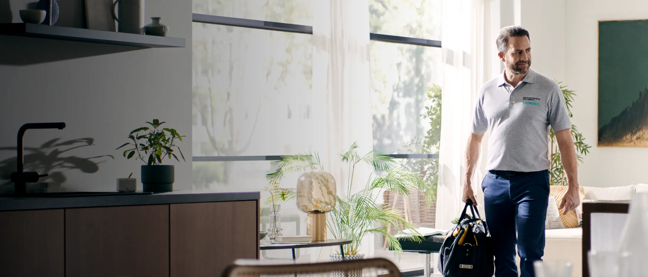 Un homme en tenue décontractée se tient dans une cuisine moderne agrémentée de plantes et d'éléments décoratifs.