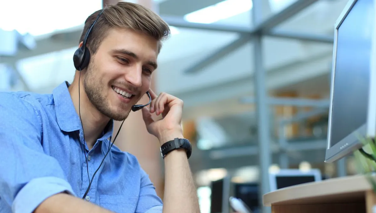 Lächelnder Mann mit Headset im Büro, telefoniert und macht sich Notizen.