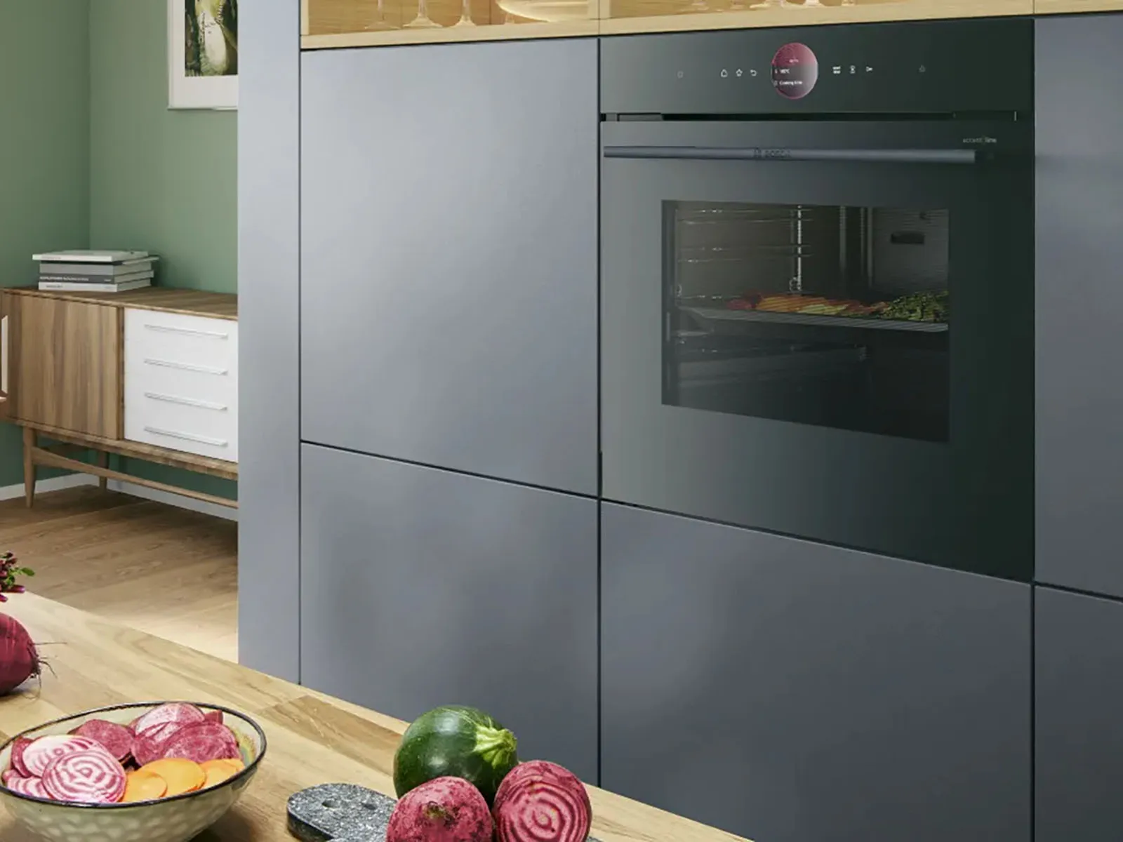 Elegant kitchen with built-in Series 8 accent line oven from Bosch with Air Fry Function and warming drawer. Various vegetables cooking in the oven. More vegetables on cutting board on a counter.