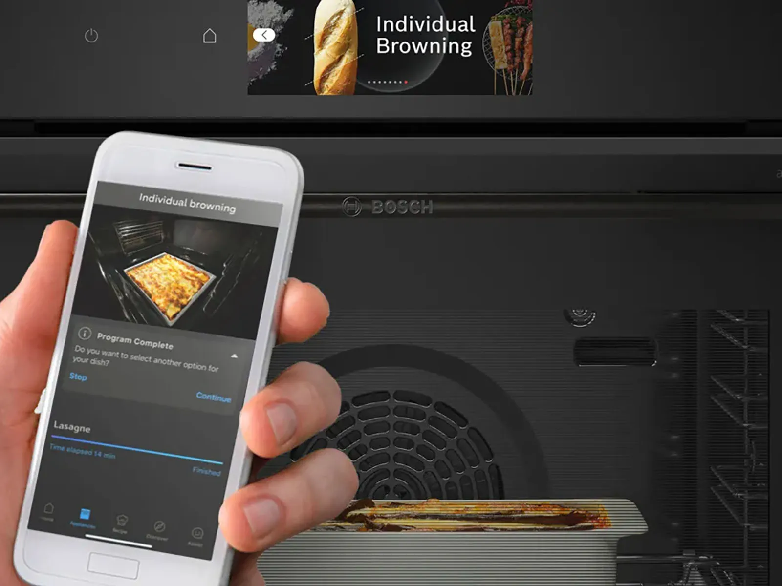 A casserole is placed in an oven. The user interface displays the programm „Individual Browning“. In front of the oven a hand holds a mobile phone which shows the inside of the oven.