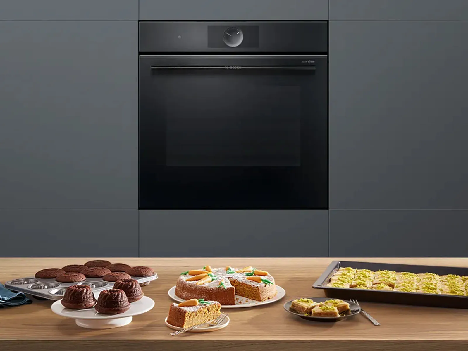 Series 8 accent line electric oven from Bosch in a kitchen. On a counter in front of it are various baked goods such as a carrot cake and muffins.