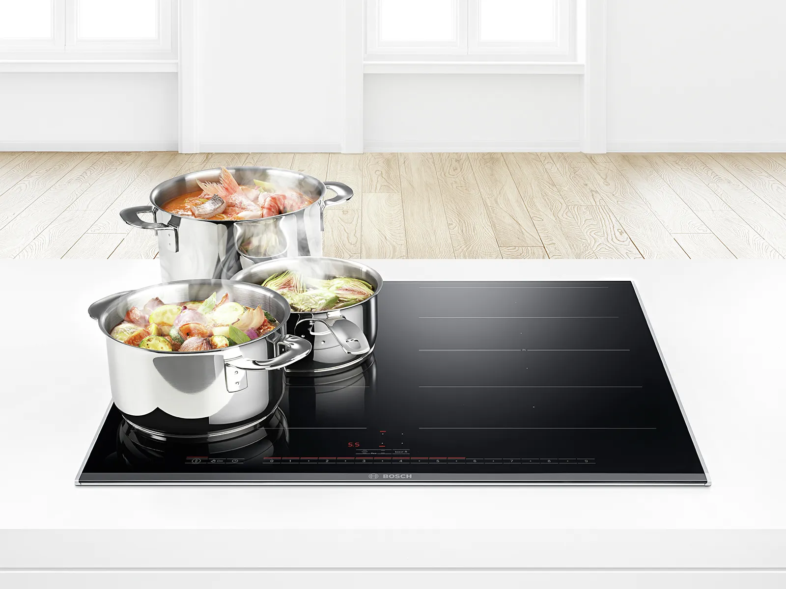 Stainless steel pots on Bosch Induction cooktop, vegetables and ingredients, modern kitchen interior.
