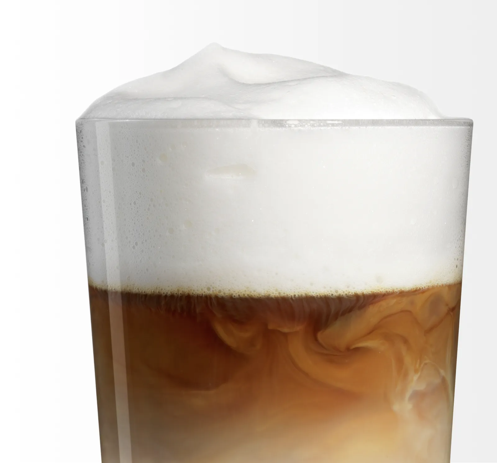Primer plano de un vaso de café helado con leche cremosa arremolinándose bajo una espesa capa de espuma.