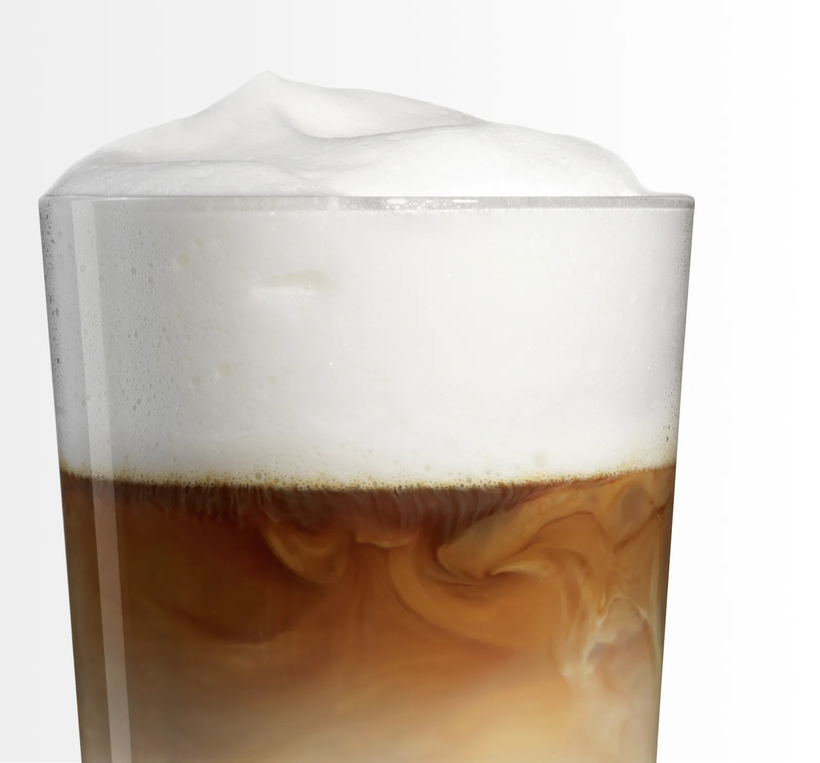 Primo piano di un bicchiere trasparente riempito con strati di caffè scuro e schiuma cremosa in cima, con bolle e vortici visibili.