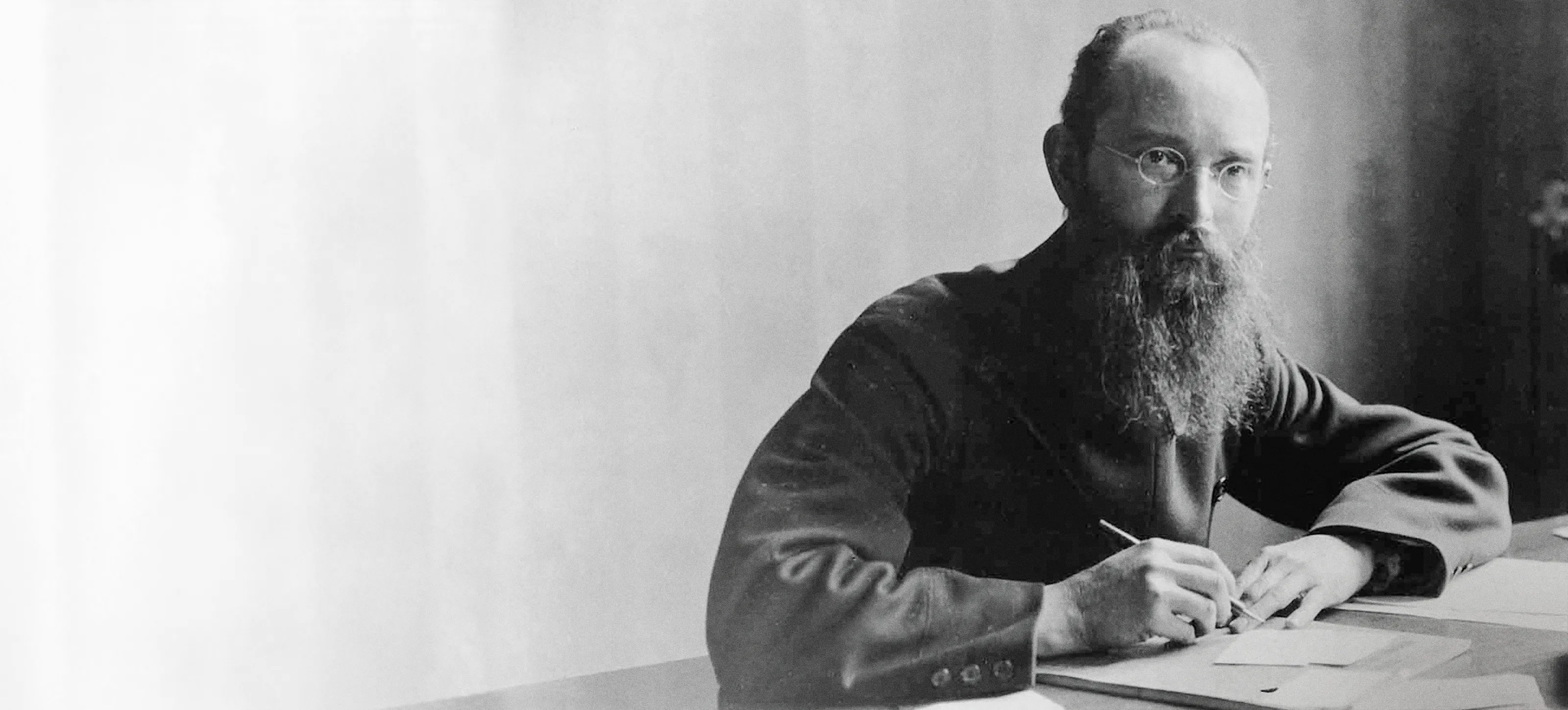 Robert Bosch with long beard, wearing dark clothing, sitting at a desk and writing.