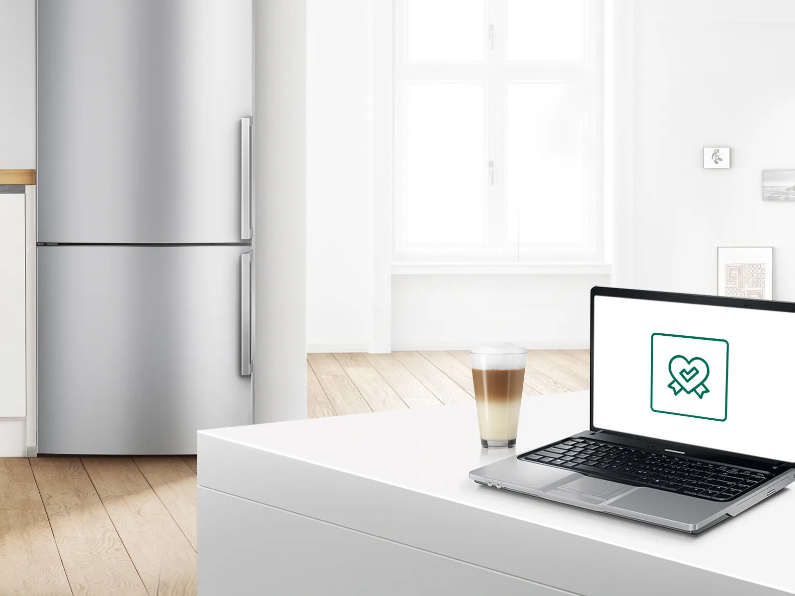 מטבח מודרני עם מקרר, מחשב נייד וקפה מוצצים על הדלפק לבן.