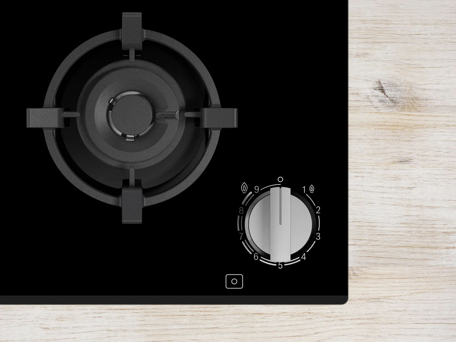 Top view of black gas stovetop burner and control knob on a light wooden surface, showcasing modern kitchen design elements.