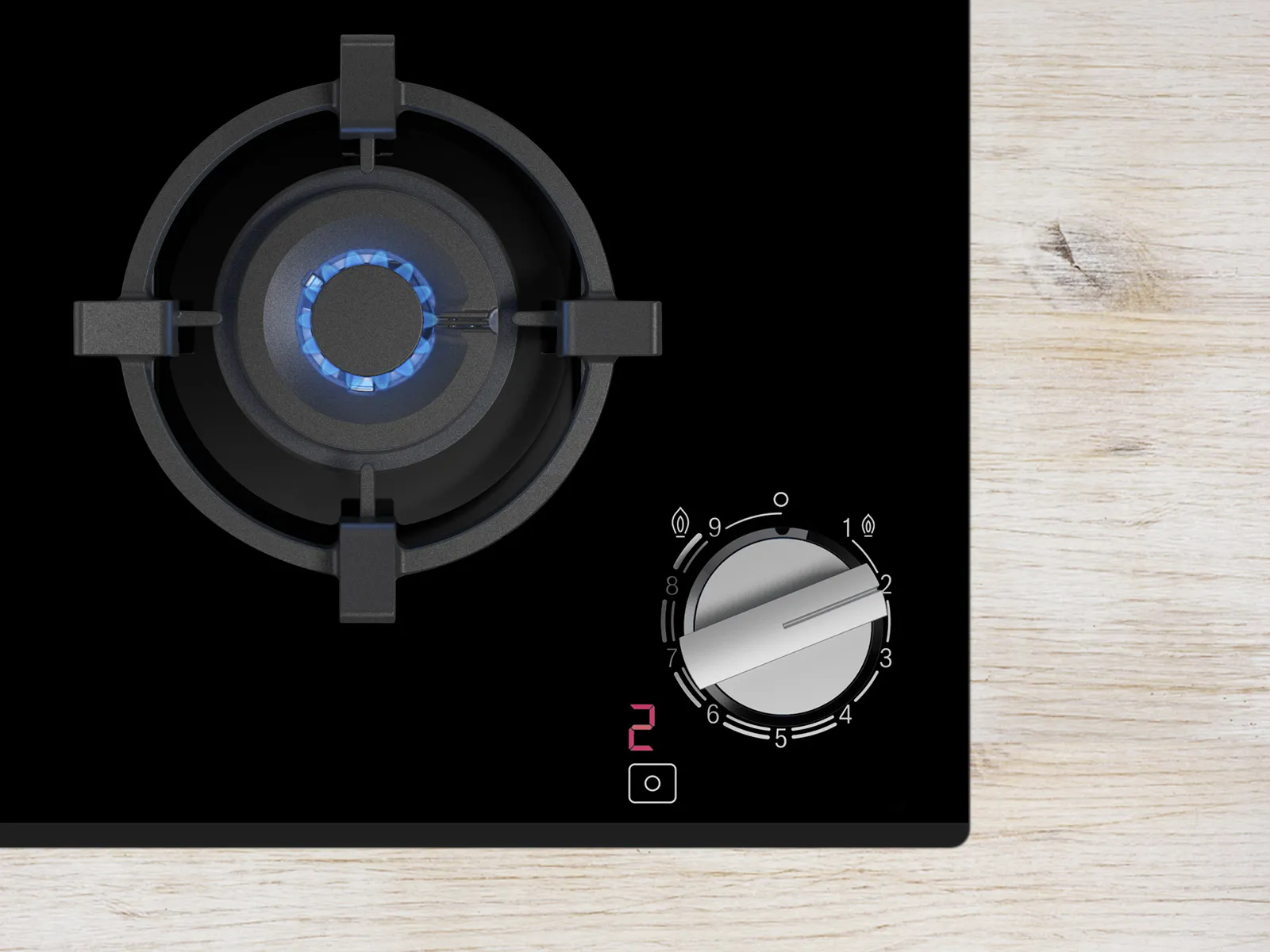 Close-up of a black gas stove with a lit burner and a control knob set to level two on a wooden surface.