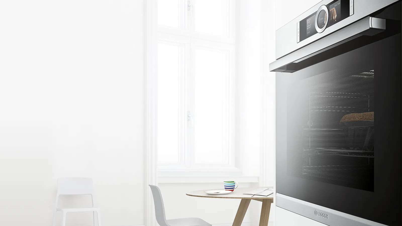 Modern kitchen setup featuring built-in oven, and a minimalist chair near a bright window.