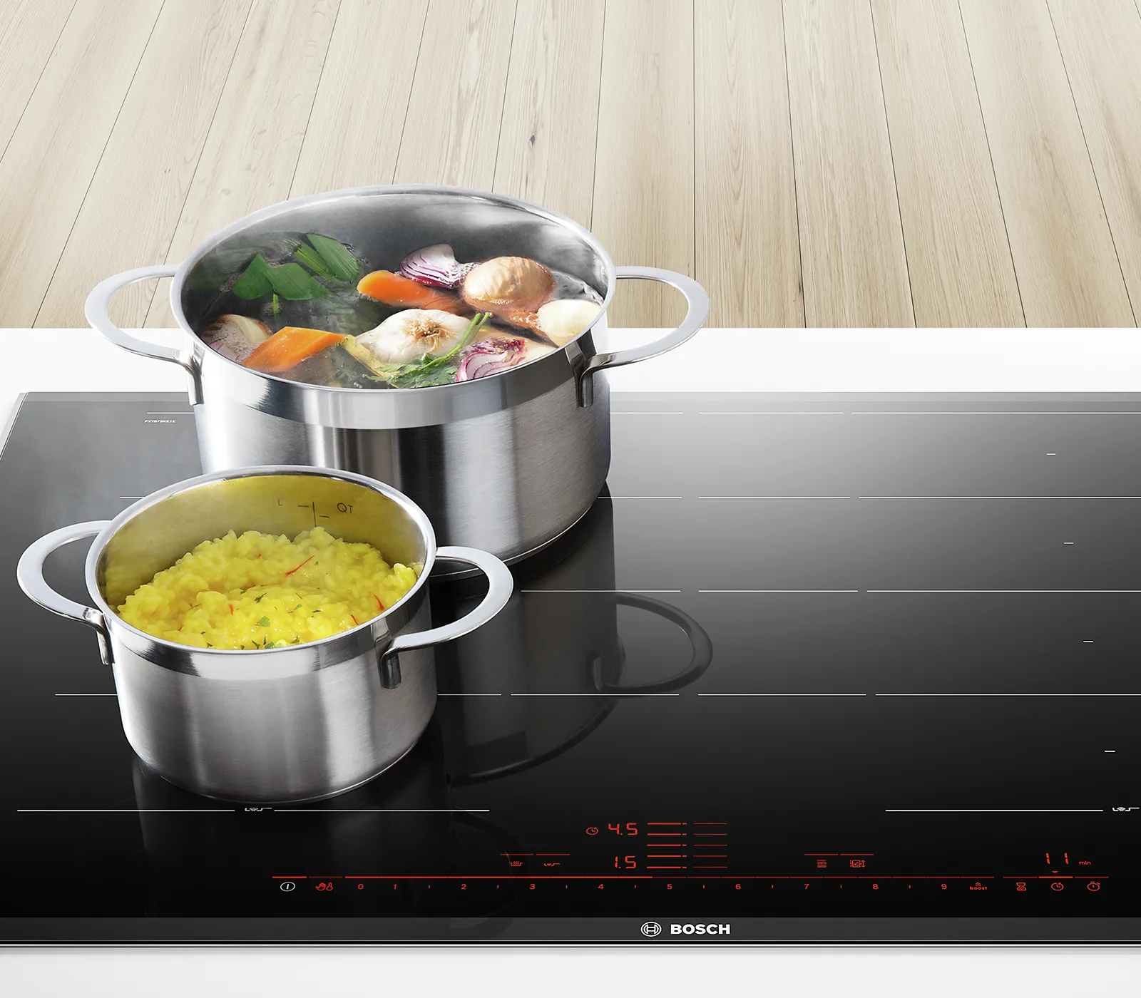 Stainless steel pots on a black induction cooktop, one containing vegetables, the other cooked rice.