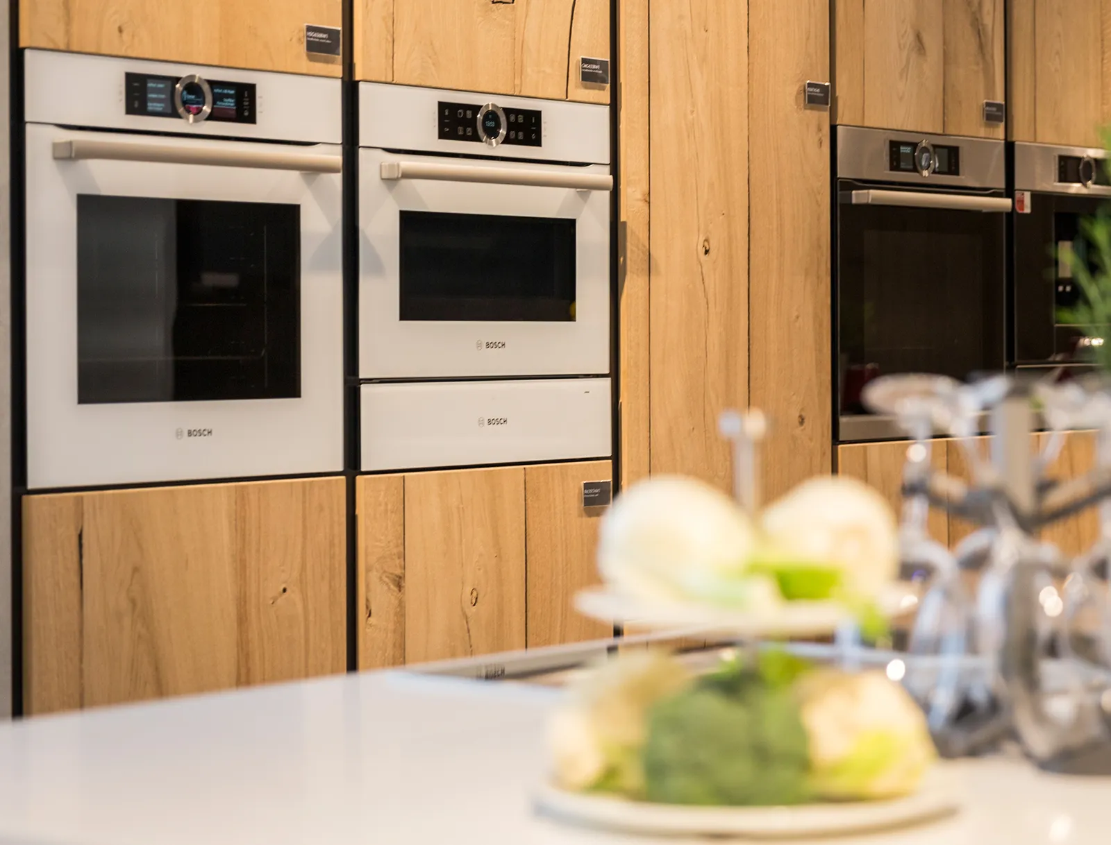Eingebaute weiße und dunkle Bosch Backöfen in einer modernen Holzküchenzeile im Showroom.