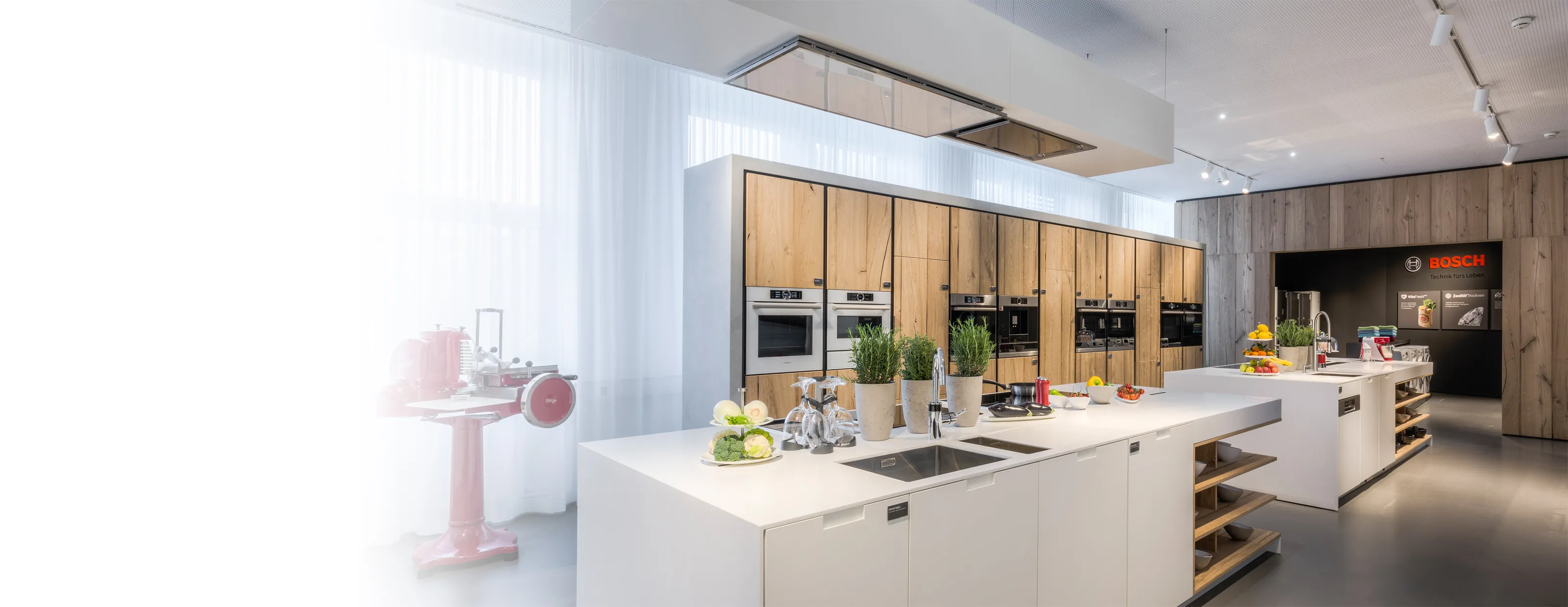Moderne Bosch Showroom-Küche mit weißen Kochinseln, Holzfronten und integrierten Einbaugeräten.
