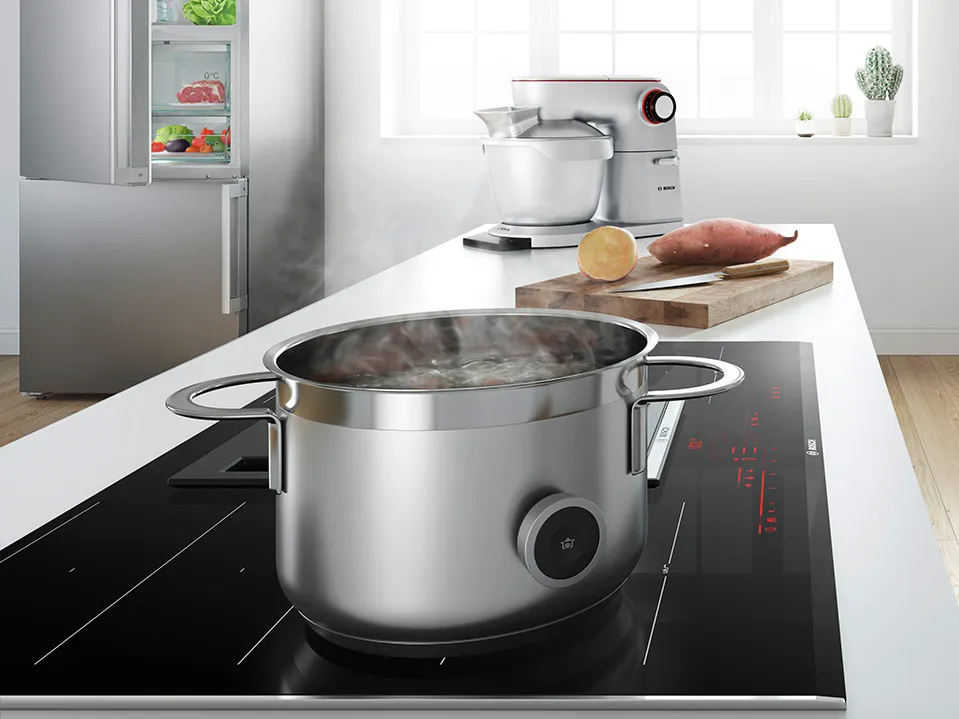 A steaming pot on an induction cooktop, with a mixer and ingredients like sweet potatoes in a modern kitchen setting.