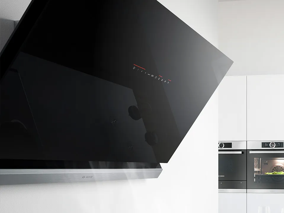 Sleek kitchen hood mounted on a white wall, with a touch of modern design and steam rising, complemented by built-in ovens.