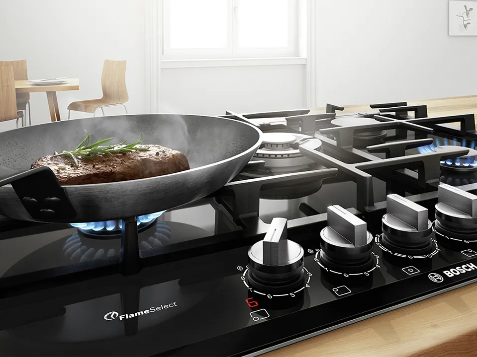 A Bosch gas stove with a sizzling steak in a pan, steam rising, and flame-select controls in a modern kitchen setting.