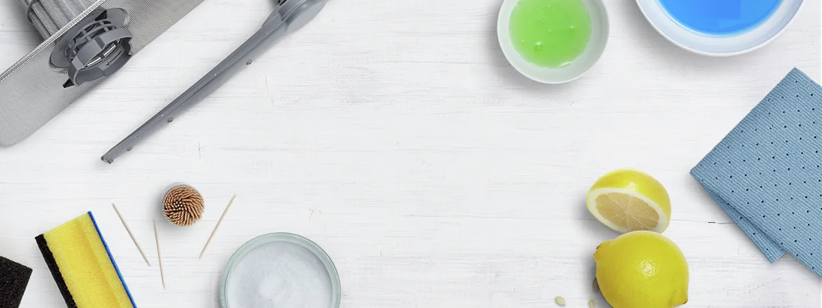 Cleaning supplies on a white surface include lemons, sponges, and bowls with liquids.