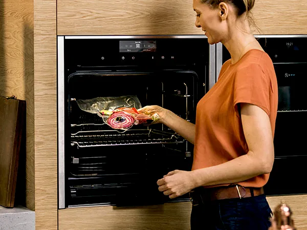 Person sliding a glass baking dish with vegetables into a built-in oven.
