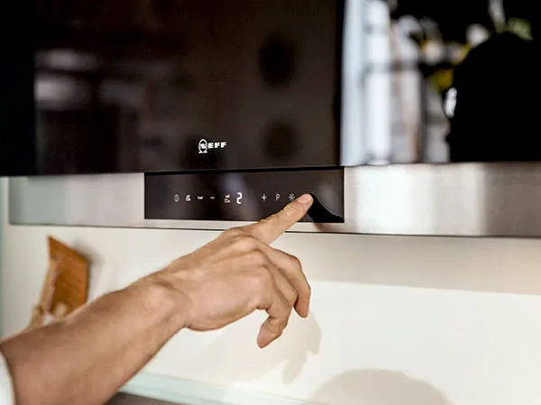 Hand adjusting controls on kitchen appliance, close-up view of control panel.