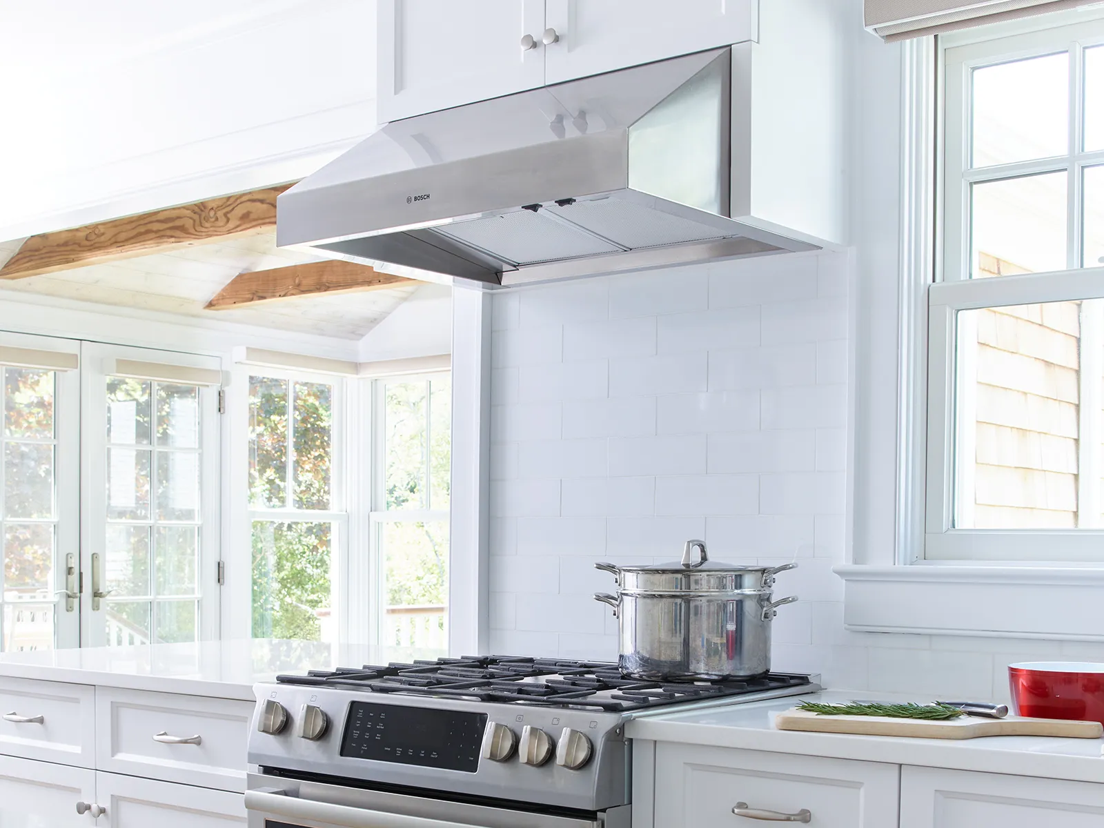 Bright, airy kitchen featuring a Bosch stainless steel range hood and gas stove.