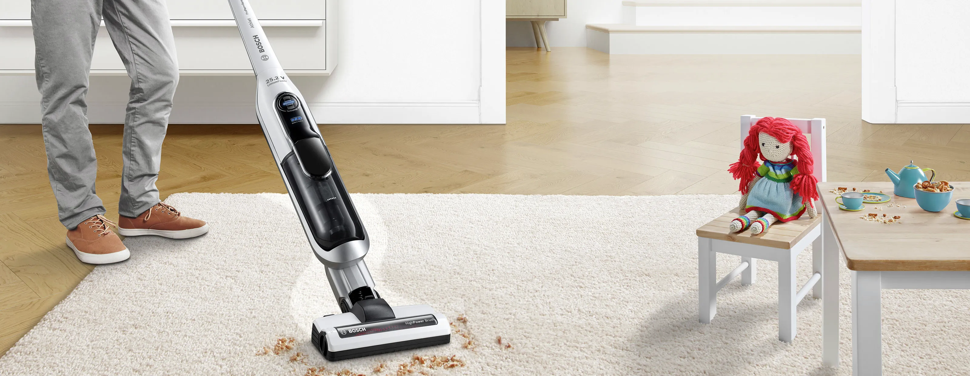 O persoană aspira murdăria de pe un covor din camera copiilor cu un aspirator vertical Bosch