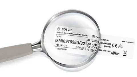 Close-up of a Bosch appliance rating label and model number magnified through a handheld magnifying glass.