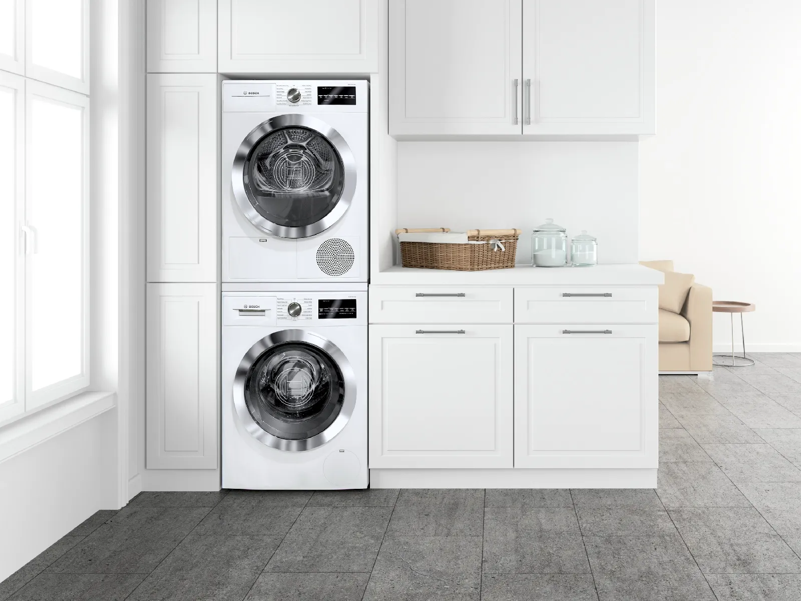Stacked Bosch white washer and dryer in modern laundry room with cabinets and large window.