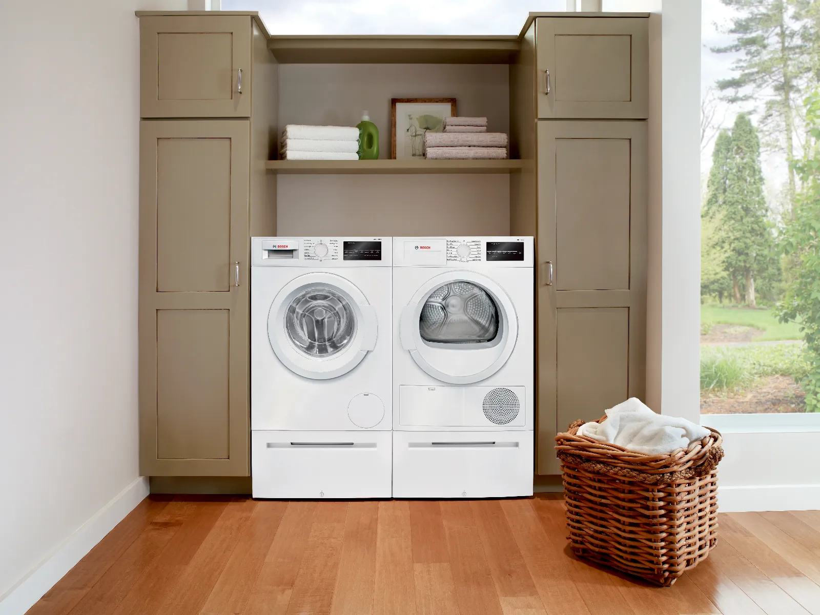 Laundry room with a Bosch washer and dryer set in white cabinets, basket on wooden floor.