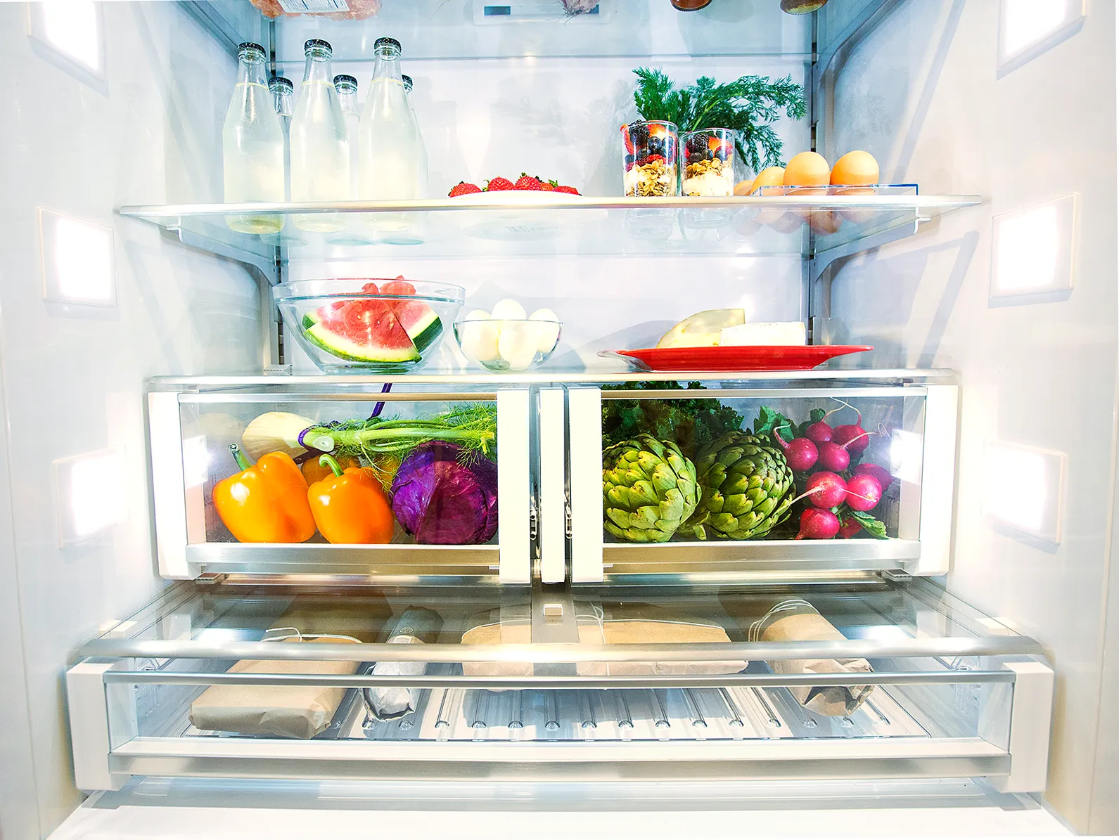 Open Bosch single door fridge filled with assorted fresh vegetables, fruits, bottles, and eggs on shelves.