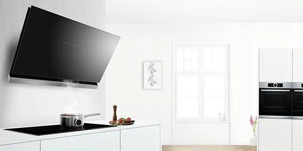 Moderne, helle Küche mit einer großen, schrägen Bosch Dunstabzugshaube aus schwarzem Glas über dem Kochfeld und integrierten Einbaugeräten im Hintergrund.