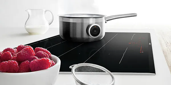 Ein Edelstahl-Stieltopf mit magnetischem PerfectCook Kochsensor auf einem modernen Bosch Induktionskochfeld neben einer Schale mit frischen Himbeeren.