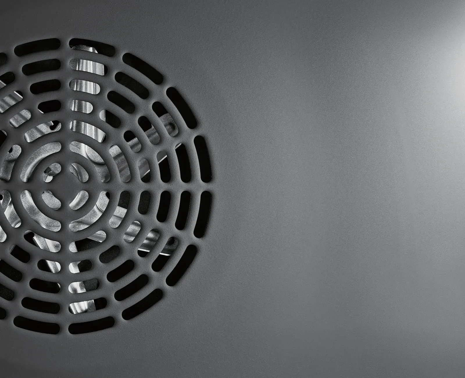 Circular metal grate against dark background, creating a minimalist, geometric pattern with negative space.