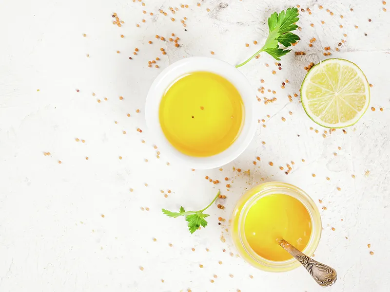 Ciotole di liquido dorato, fetta di limone, prezzemolo e spezie su uno sfondo bianco.