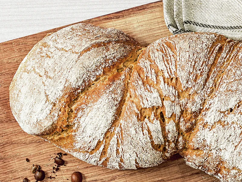 Pane artigianale appena cotto, esterno croccante, tavola di legno, chicchi di caffè.