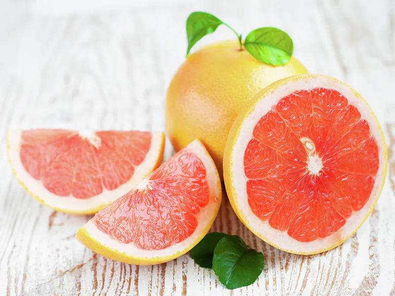 Vibrante pompelmo metà e fette su superficie di legno, con foglie verdi.