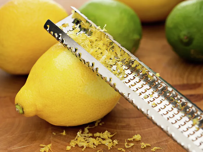 Limoni, lime e una grattugia di metallo su una superficie di legno, mostrando il processo di agrumi zesting.