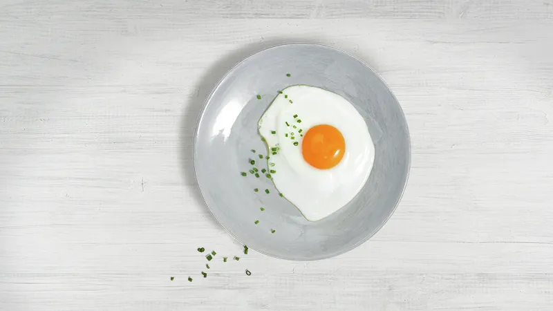 A fried egg with chives on a gray plate, placed on a white wooden surface.